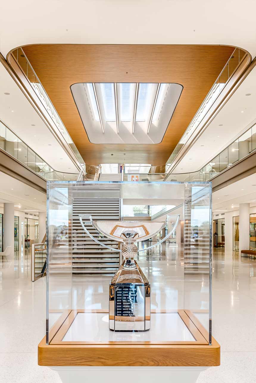 A closeup of a trophy in a glasscase. Visible in the back is the atrium's central staircase and large skylights.