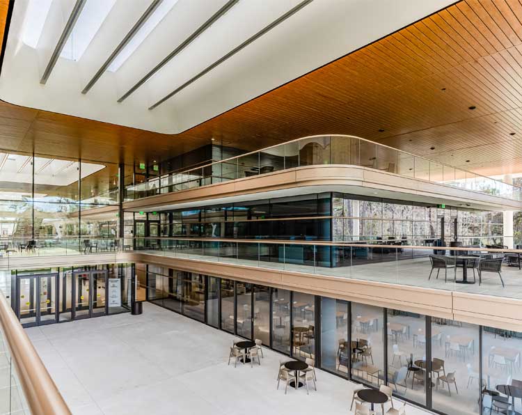 A shot of the entrance courtyard at PGA Tour HQ, light woods, and curved lines define the space, with multiple levels of outdoor seating under a wooden ceiling that protects from the Florida elements