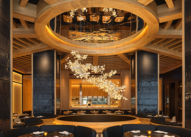 A shot of Nobu Toronto's main dining room, looking towards the partially exposed kitchen where a chef works