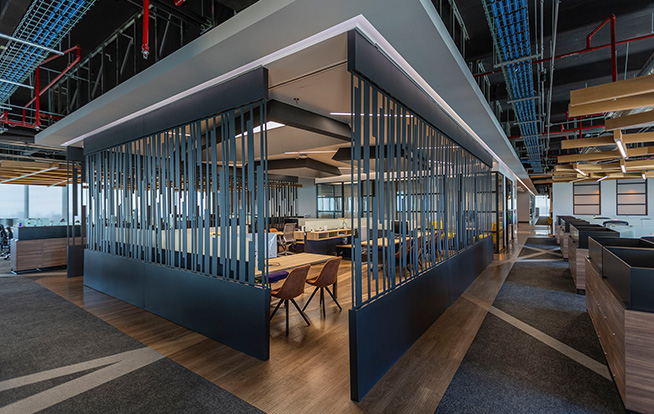 A semi-enclosed office space with styled grates lining it. On the exterior are more desks and on the ground the same criss-crossed line motif from the ceiling carries through