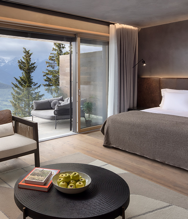 A luxury hotel room at the Six Senses Crans Montana. The drapes are open to reveal a terrace and beautiful view of the mountains.
