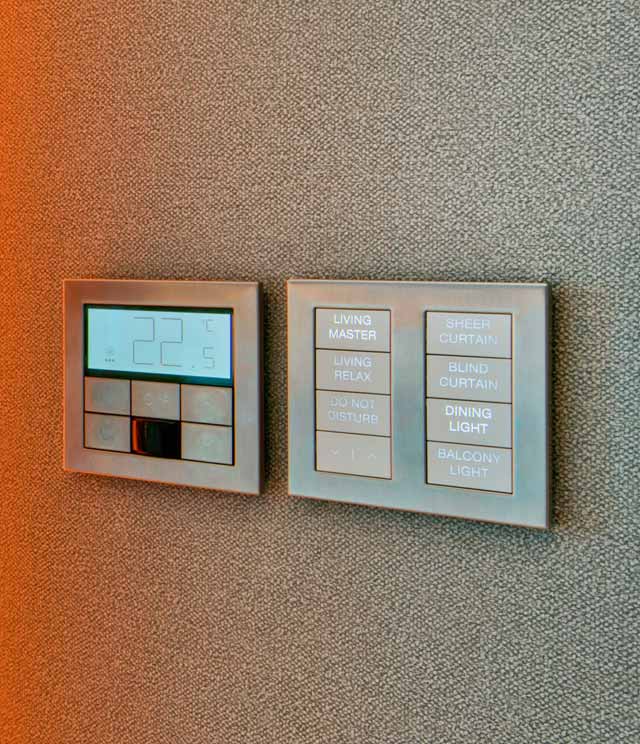 A close up of a metal Palladiom keypad and a matching Palladiom thermostat on the wall of a hotel room. 