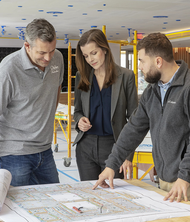 A woman and two men review blueprints at a table on a commercial project. 